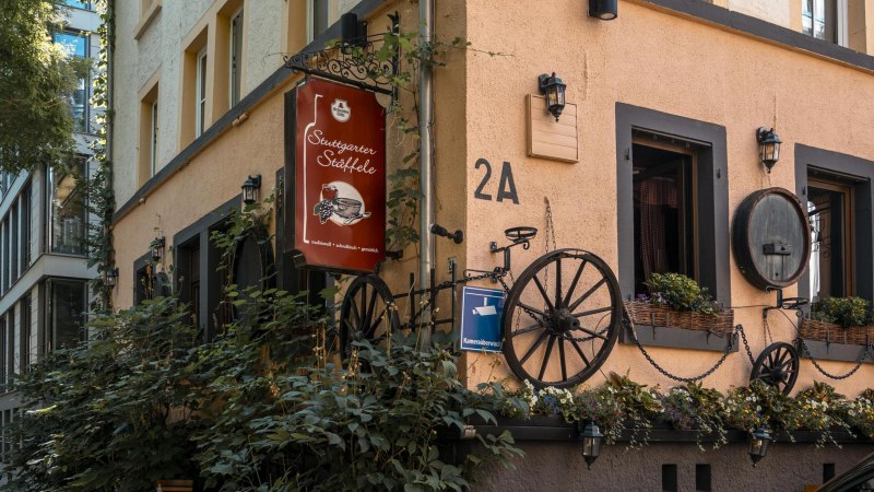 Gebäude mit Schild 'Stuttgarter Stäffele', dekoriert mit Pflanzen und alten Wagenrädern. Adresse 2A, Überwachungskamera-Schild sichtbar., © SMG, Sarah Schmid