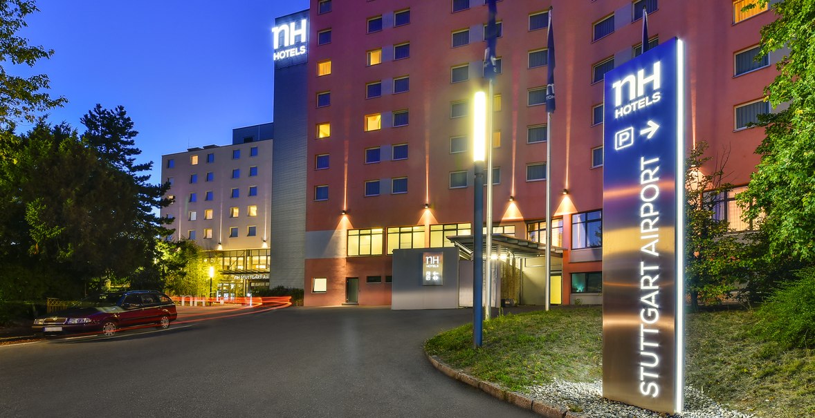 Beleuchtetes NH Hotel bei Nacht mit Schild 'Stuttgart Airport'. Geb&auml;ude mit vielen Fenstern, umgeben von B&auml;umen., &copy; NH Hotel Stuttgart Airport