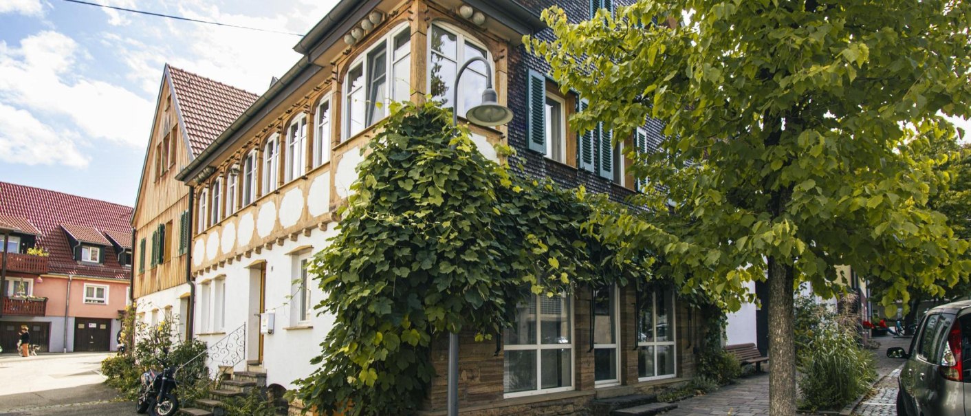 Historic half-timbered house in Bad Boll, overgrown with ivy. A tree and a car can be seen in the foreground. The sky is slightly cloudy., © Stuttgart-Marketing GmbH, Sarah Schmid