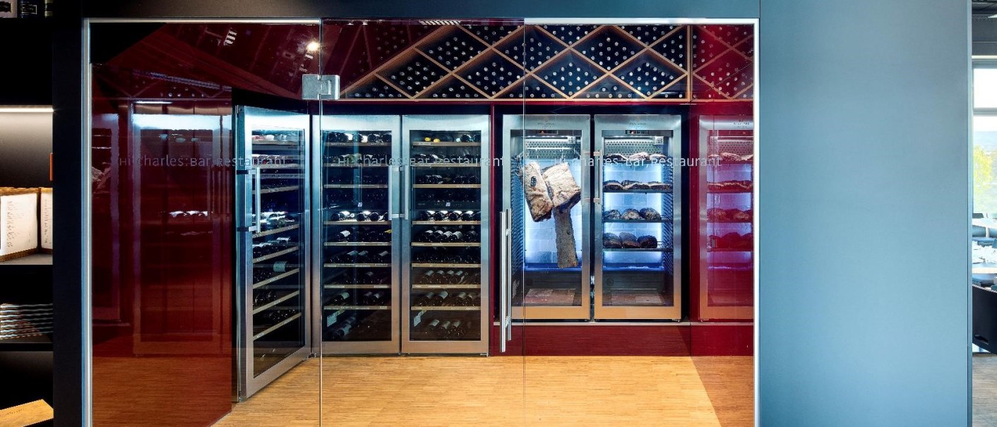 Glass front of the "Hi, Charles" restaurant with wine racks and bread display in the background. Modern design with wooden floor., © Hotel am Remspark Glass front of the "Hi, Charles" restaurant with wine racks and bread display in the background. Modern design with wooden floor., © Hotel am Remspark