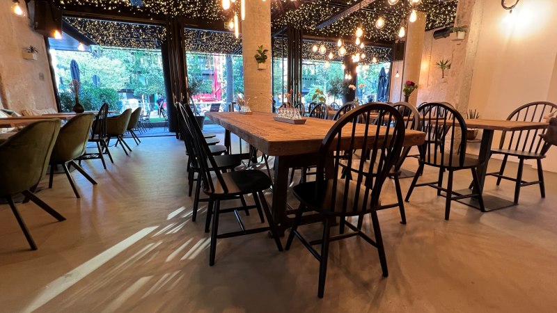 Ein stilvoll eingerichtetes Restaurant mit Holztischen, schwarzen St&uuml;hlen und einer Decke voller Lichterketten., &copy; heavenskitchen