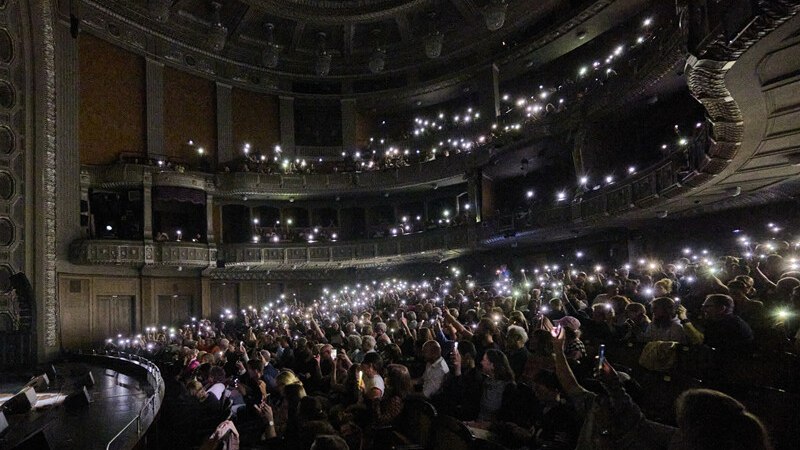 A packed theater with an audience holding up glowing cell phones creates an atmospheric ambiance. The architecture is classic and impressive., &copy; W&uuml;rttembergische Staatstheater Stuttgart