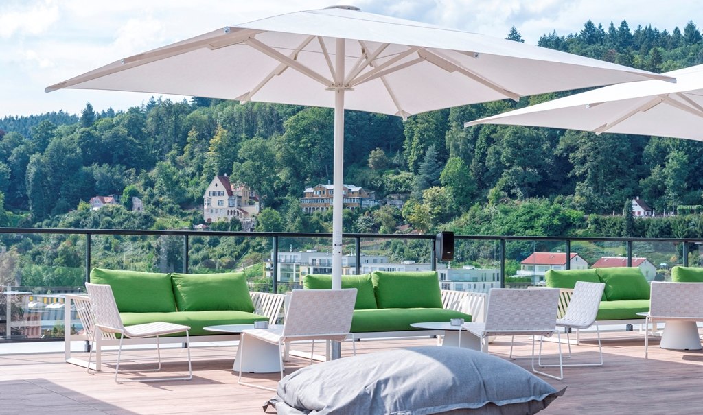 Modern roof terrace with green sofas, white parasols and views of wooded hills and houses., &copy; Hotel am Remspark