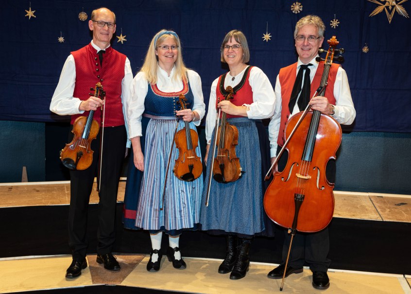 Vier Musiker in traditioneller Kleidung halten Streichinstrumente. Sie stehen vor einem blauen Hintergrund mit Sternendekoration., © Peter Oehl