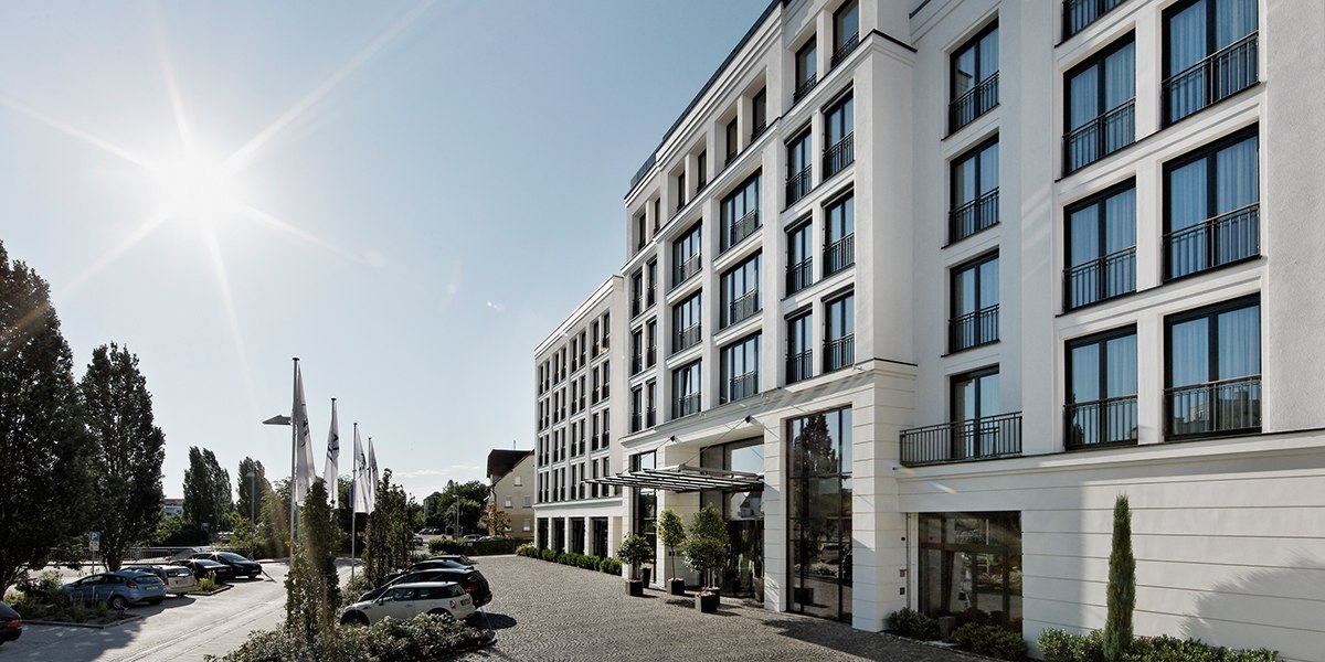 Modern building façade with large windows, sunny sky, cars and flags in the foreground., © Parkhotel Stuttgart Messe-Airport Modern building façade with large windows, sunny sky, cars and flags in the foreground., © Parkhotel Stuttgart Messe-Airport