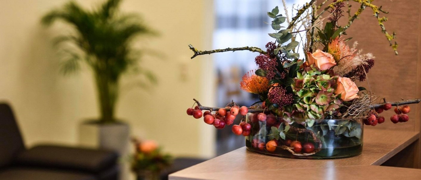 Flower arrangement in glass vase on reception counter, couch and plant in the background., © TOMAS Flower arrangement in glass vase on reception counter, couch and plant in the background., © TOMAS