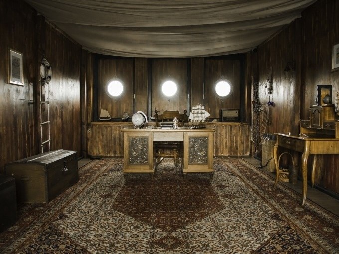 Rustic ship interior with wooden walls, desk, globe and model ship. Three portholes on the wall., © ExitGames Stuttgart Rustic ship interior with wooden walls, desk, globe and model ship. Three portholes on the wall., © ExitGames Stuttgart
