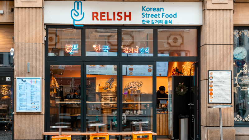 Das Bild zeigt die Fassade des Restaurants 'Relish', das koreanisches Street Food anbietet. Die Glasfront ist mit Neonlichtern dekoriert., &copy; Stuttgart-Marketing GmbH, Sarah Schmid
