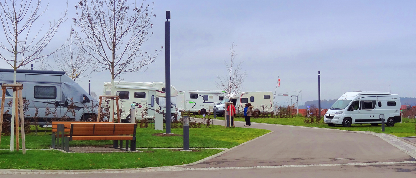 Wohnmobilstellplatz mit mehreren Wohnmobilen, kahlen Bäumen und einer Bank. Zwei Personen stehen auf dem Weg. Trübes Wetter., © Panorama Therme Beuren, Birgit Eschment