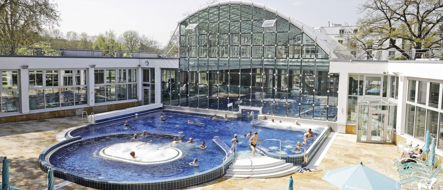 The SoleBad Bad Cannstatt features a modern swimming pool with a glass façade. People relax in the water and on sun loungers., © Stuttgarter Bäder The SoleBad Bad Cannstatt features a modern swimming pool with a glass façade. People relax in the water and on sun loungers., © Stuttgarter Bäder