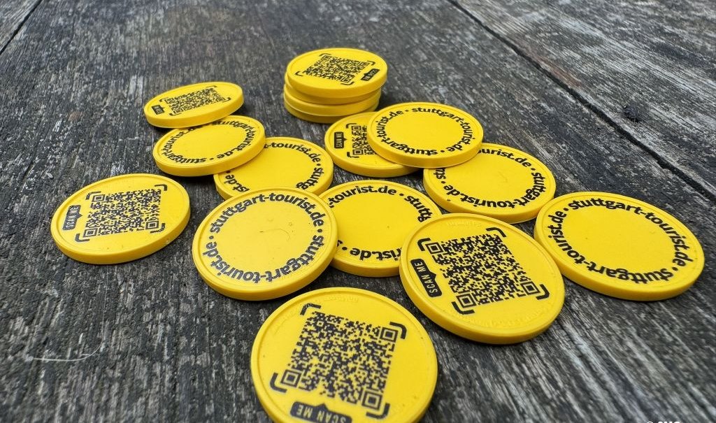 Gelbe Chips mit QR-Codes und der Aufschrift stuttgart-tourist.de liegen auf einem Holztisch verstreut., © SMG