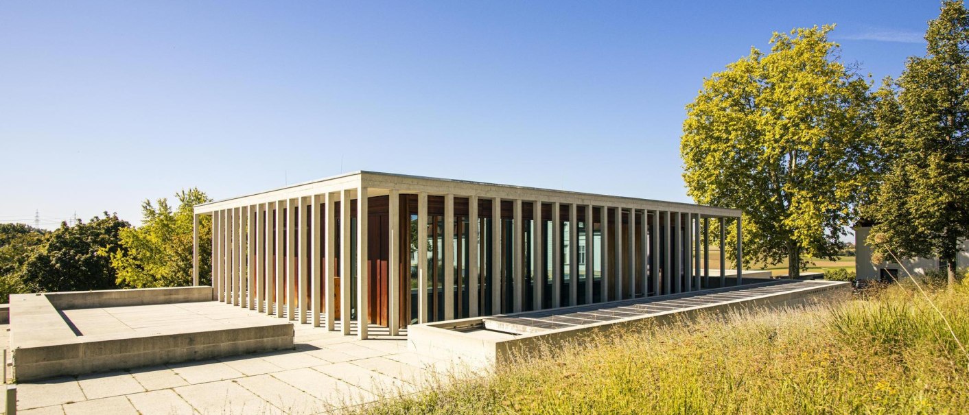 A modern building with a glass facade and columns, surrounded by trees and a meadow under a clear sky., &copy; SMG Stuttgart Marketing GmbH - Sarah Schmid