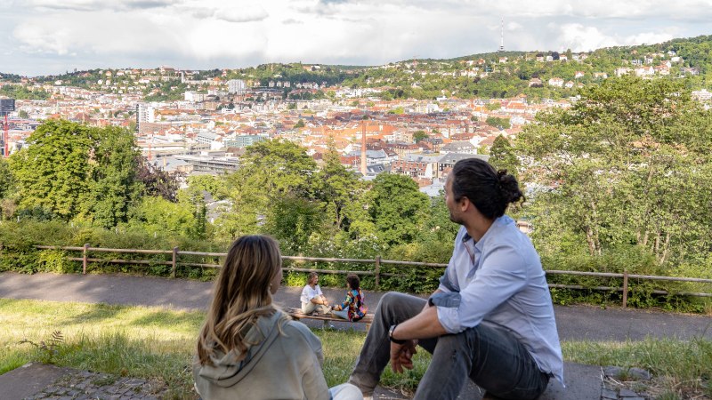 Two people sit on a meadow and look out over the city of Stuttgart. Hills and buildings can be seen in the background, including the television tower., &copy; SMG, Martina Denker
