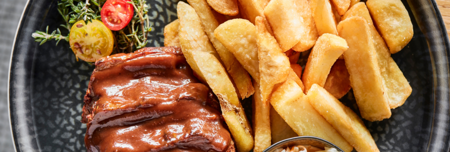 A plate of juicy ribs in sauce, crispy chips and a portion of coleslaw, garnished with herbs and tomatoes., © MAREDO
