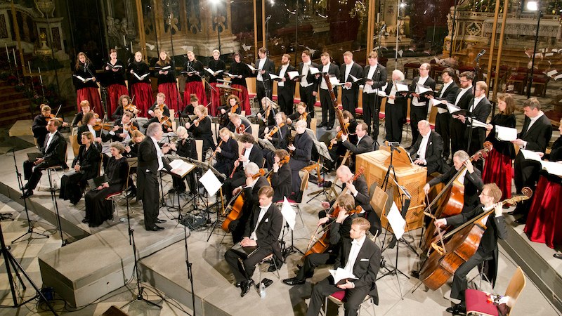 Ein Orchester und Chor in formeller Kleidung führen ein klassisches Musikstück in einer prunkvollen Kirche auf. Die Musiker sind konzentriert bei der Arbeit., © Musik Podium Stuttgart e.V. Ein Orchester und Chor in formeller Kleidung führen ein klassisches Musikstück in einer prunkvollen Kirche auf. Die Musiker sind konzentriert bei der Arbeit., © Musik Podium Stuttgart e.V.