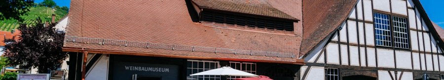 Visitors stand in front of the wine museum in Uhlbach. The half-timbered building has a red tiled roof. Vineyards can be seen in the background., © Stuttgart-Marketing GmbH, Thomas Niedermüller