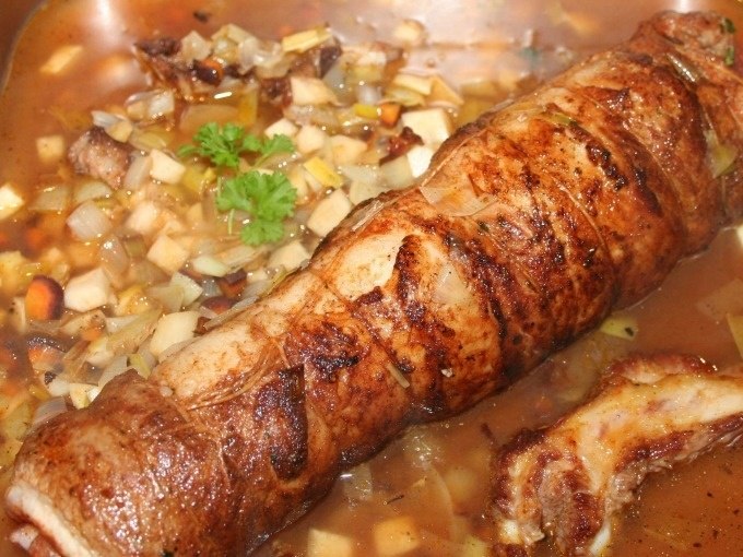 Ein gerollter Braten in einer Pfanne, umgeben von Gem&uuml;sew&uuml;rfeln und einer braunen Sauce, garniert mit einem Petersilienzweig., &copy; Kultweine-Kochwelten-Kunst&uuml;cke - Kochschule Sonja Lenz