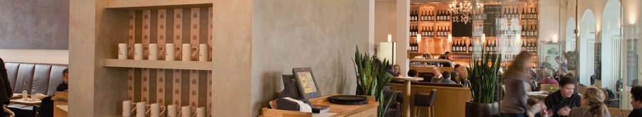 Stylish restaurant with wooden furniture, shelves full of cups and a cozy atmosphere. Guests sit at tables, with a bar in the background., &copy; Aspectus Photographie Stuttgart