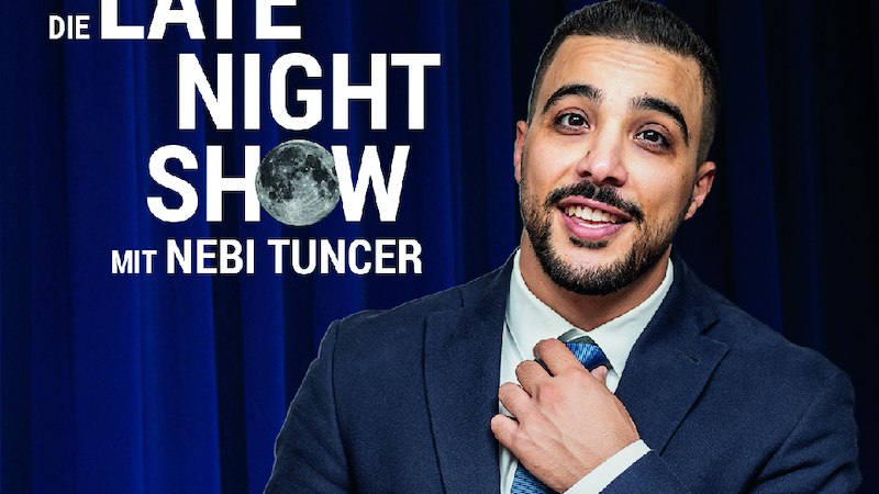 A man in a suit stands in front of a blue curtain. The words 'The Late Night Show with Nebi Tuncer' can be seen., &copy; SBEntertainment GmbH & Co.KG
