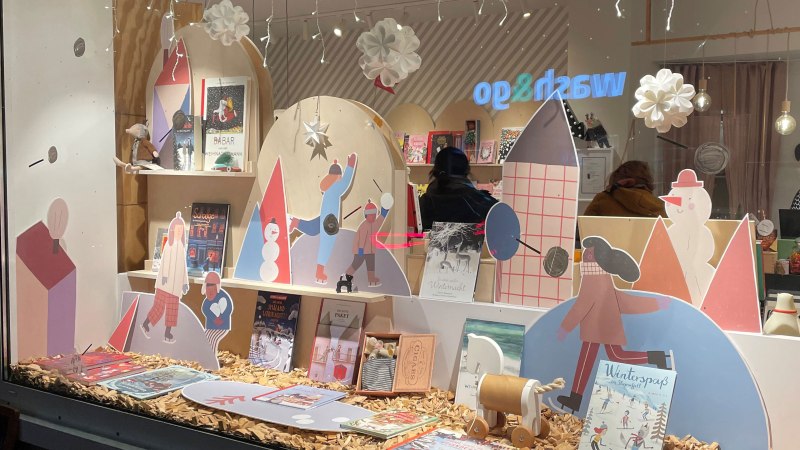 Ein Schaufenster mit winterlicher Dekoration, Kinderbüchern und Pappfiguren. Lichterketten und Schneeflocken hängen von der Decke., © Stuttgart-Marketing GmbH