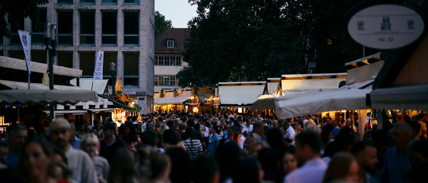 A dense crowd at the Stuttgart Wine Festival in 2025, surrounded by illuminated booths at dusk., © Pro Stuttgart e.V. A dense crowd at the Stuttgart Wine Festival in 2025, surrounded by illuminated booths at dusk., © Pro Stuttgart e.V.