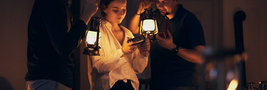 Three people are standing in a dark room holding lanterns. They are looking together at a small object that one of them is holding., &copy; Julia Ochs