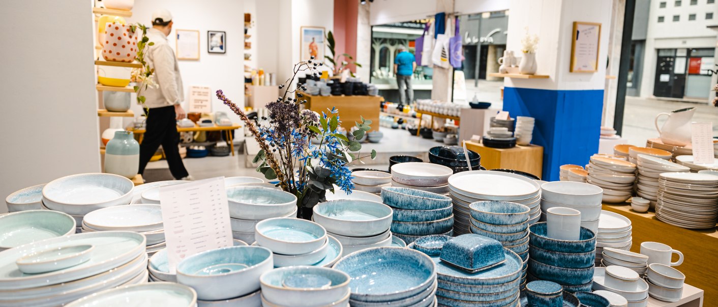 Ein Geschäft mit buntem Keramikgeschirr auf Regalen. Teller und Schalen in verschiedenen Farben. Ein Mann geht im Hintergrund vorbei., © SMG Stuttgart Marketing GmbH - Sarah Schmid