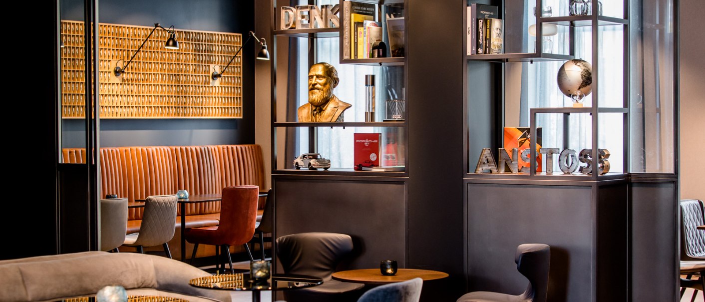 Moderne Lounge mit gemütlichen Sitzgelegenheiten, Bücherregalen und Dekorationen wie einer Büste und einem Globus. Elegantes, stilvolles Ambiente., © TOMAS