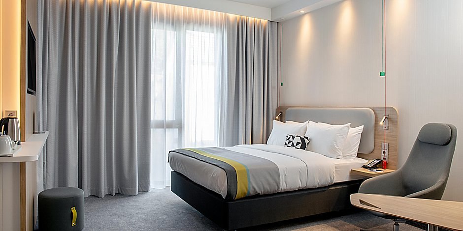 Modernes Hotelzimmer mit Doppelbett, grauen Vorhängen, Sessel und Schreibtisch. Dezente Beleuchtung und neutrale Farben dominieren den Raum., © Holiday Inn Express Waiblingen Modernes Hotelzimmer mit Doppelbett, grauen Vorhängen, Sessel und Schreibtisch. Dezente Beleuchtung und neutrale Farben dominieren den Raum., © Holiday Inn Express Waiblingen