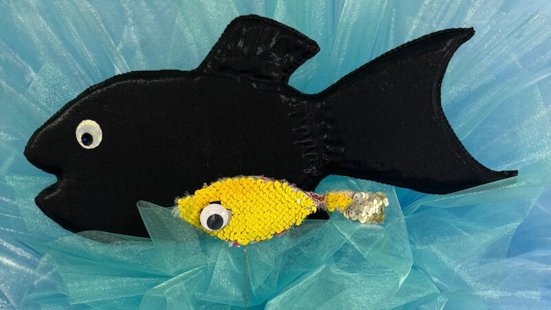 Ein schwarzer Stofffisch und ein kleiner gelber Paillettenfisch auf blauem Hintergrund aus Stoff., © FITZ Das Theater animierter Formen Ein schwarzer Stofffisch und ein kleiner gelber Paillettenfisch auf blauem Hintergrund aus Stoff., © FITZ Das Theater animierter Formen