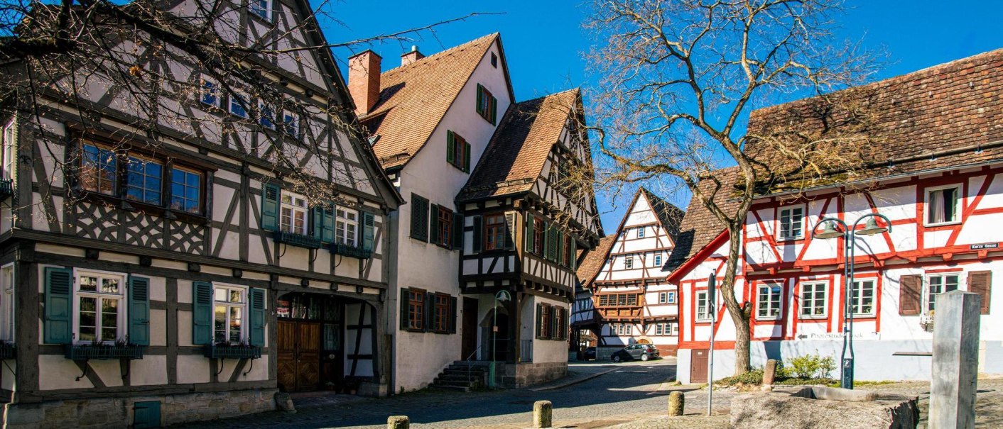 Half-timbered houses in the old town of Sindelfingen, shining under a blue sky. A tree without leaves stands in the foreground., © Stuttgart-Marketing GmbH, Sarah Schmid Half-timbered houses in the old town of Sindelfingen, shining under a blue sky. A tree without leaves stands in the foreground., © Stuttgart-Marketing GmbH, Sarah Schmid