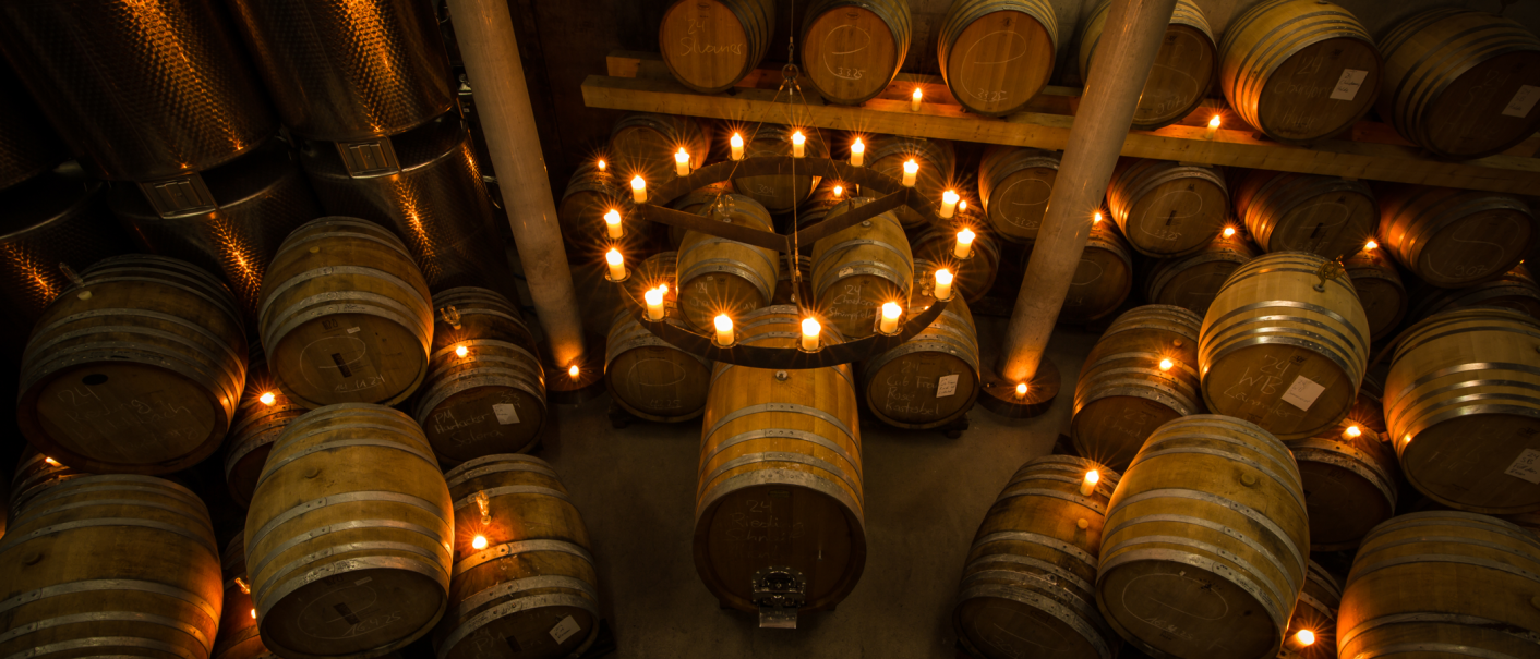 Ein stimmungsvoller Weinkeller mit Holzfässern und einem großen Kerzenleuchter in der Mitte, der warmes Licht verbreitet., © Weingut Schnaitmann