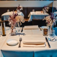 Ein elegant gedeckter Tisch in einem Restaurant mit wei&szlig;en Tischdecken, Blumenarrangement, Gl&auml;sern und Besteck., &copy; Feinkost B&ouml;hm GmbH