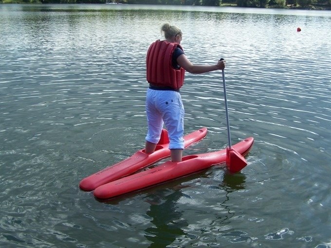 Person with life jacket stands on red water shoes and paddles on a lake., &copy; Cool-Tours StattReisen