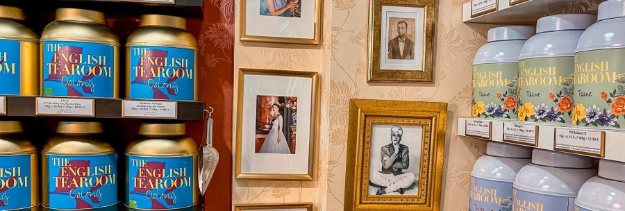 Shelves with tea caddies from 'The English Tearoom' and framed photos on a decorative wall., © Tea Room, Stuttgart