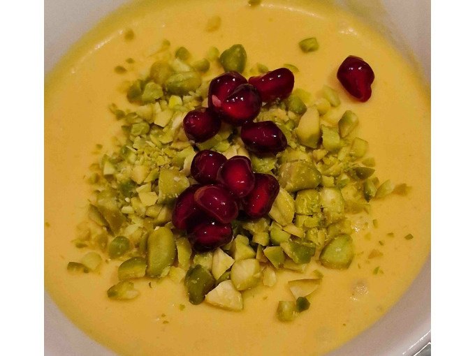 Ein cremiges gelbes Dessert, garniert mit gehackten Pistazien und Granatapfelkernen, pr&auml;sentiert sich in einer Schale., &copy; Kultweine-Kochwelten-Kunst&uuml;cke - Kochschule Sonja Lenz
