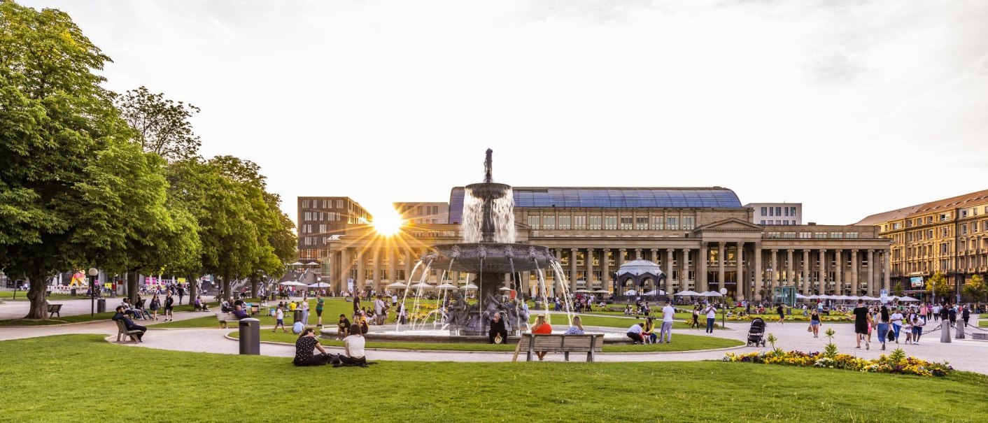 Schlossplatz in Stuttgart bei Sonnenuntergang, Menschen entspannen sich auf der Wiese, im Hintergrund der Königsbau und ein Brunnen., © Stuttgart-Marketing GmbH, Werner Dieterich Schlossplatz in Stuttgart bei Sonnenuntergang, Menschen entspannen sich auf der Wiese, im Hintergrund der Königsbau und ein Brunnen., © Stuttgart-Marketing GmbH, Werner Dieterich