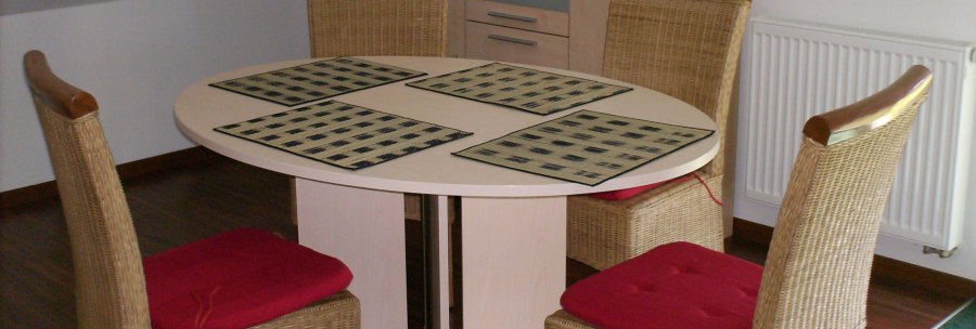 Esszimmer mit rundem Tisch, vier geflochtenen Stühlen mit roten Kissen, Platzsets und einer Anrichte mit Getränken in einer Ferienwohnung., © Weinhof am Württemberg Esszimmer mit rundem Tisch, vier geflochtenen Stühlen mit roten Kissen, Platzsets und einer Anrichte mit Getränken in einer Ferienwohnung., © Weinhof am Württemberg