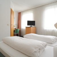 A hotel room with two single beds, a TV on a wardrobe, a desk with chair and large windows with curtains., &copy; TOMAS