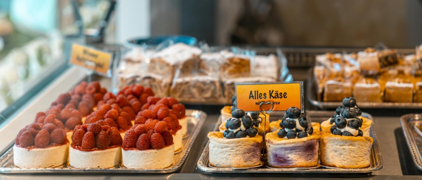 Kuchen in einer Vitrine, dekoriert mit Himbeeren und Blaubeeren. Ein Schild mit der Aufschrift 'Alles Käse' ist sichtbar., © Stuttgart-Marketing GmbH, Sarah Schmid