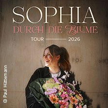 Eine lächelnde Frau hält einen Blumenstrauß. Im Hintergrund steht "SOPHIA - Durch die Blume Tour 2026". Foto von Paul Hüttemann., © links im Bild