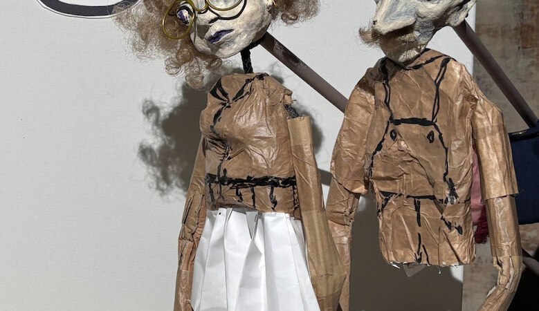 Zwei kunstvoll gestaltete Puppen aus Papier und Pappe stehen vor einem Schild mit einem 'H'. Die Puppen haben ausdrucksstarke Gesichter und detaillierte Kleidung., &copy; FITZ Das Theater animierter Formen