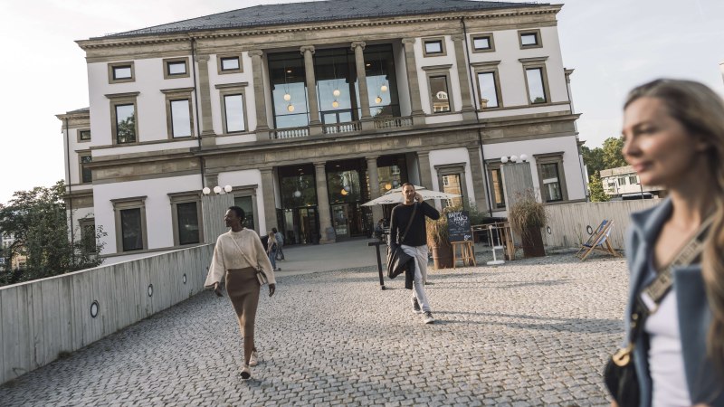 Das StadtPalais Stuttgart mit klassischer Fassade, Menschen gehen auf einem gepflasterten Weg davor. Im Hintergrund sind Bäume und ein sonniger Himmel., © Stuttgart-Marketing GmbH, WP Steinheisser