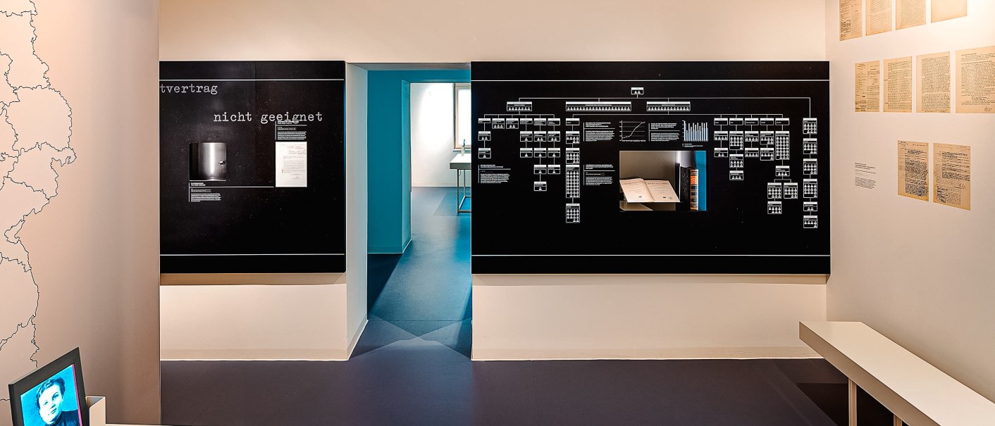 Ein Ausstellungsraum im Hotel Silber mit Informationstafeln, historischen Dokumenten und einer Karte. Ein Bildschirm zeigt ein Porträtfoto., © Daniel Stauch