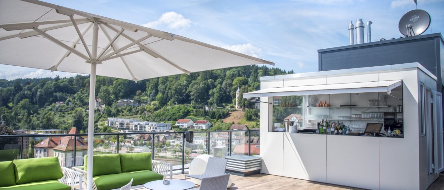 Modern roof terrace bar with parasol, green sofas and a view of a green hilly landscape., &copy; Hotel am Remspark