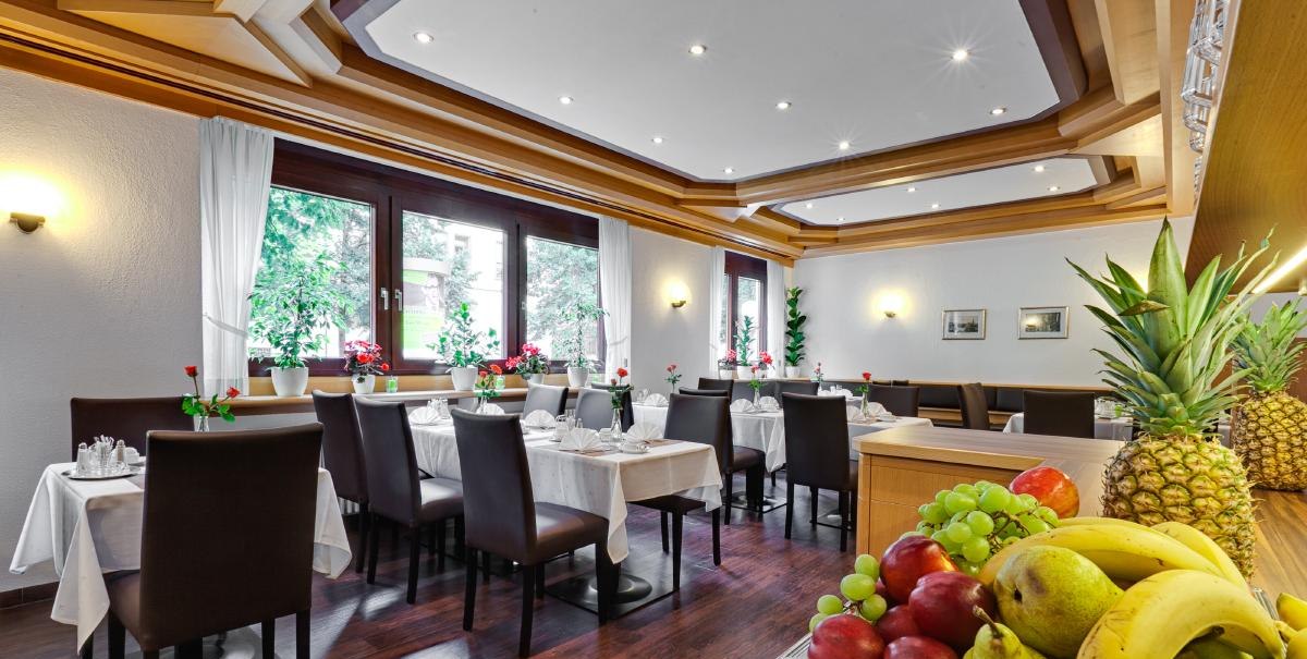 Eleganter Fr&uuml;hst&uuml;cksraum mit gedeckten Tischen, dunklen St&uuml;hlen und einer Obstschale im Vordergrund. Gro&szlig;e Fenster lassen viel Licht herein., &copy; ARNOTEL GmbH