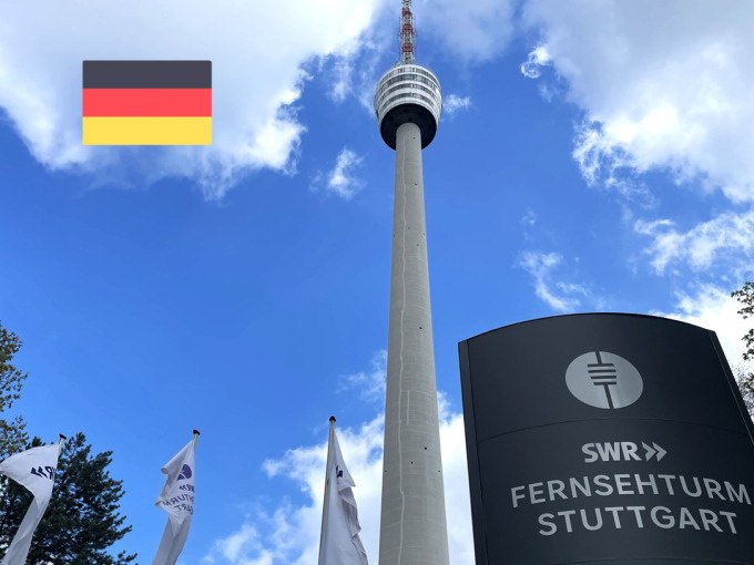 Der Fernsehturm Stuttgart ragt in den blauen Himmel, umgeben von Fahnen. Eine deutsche Flagge ist oben links im Bild zu sehen., &copy; SWR Media Services GmbH / Fernsehturm Stuttgart
