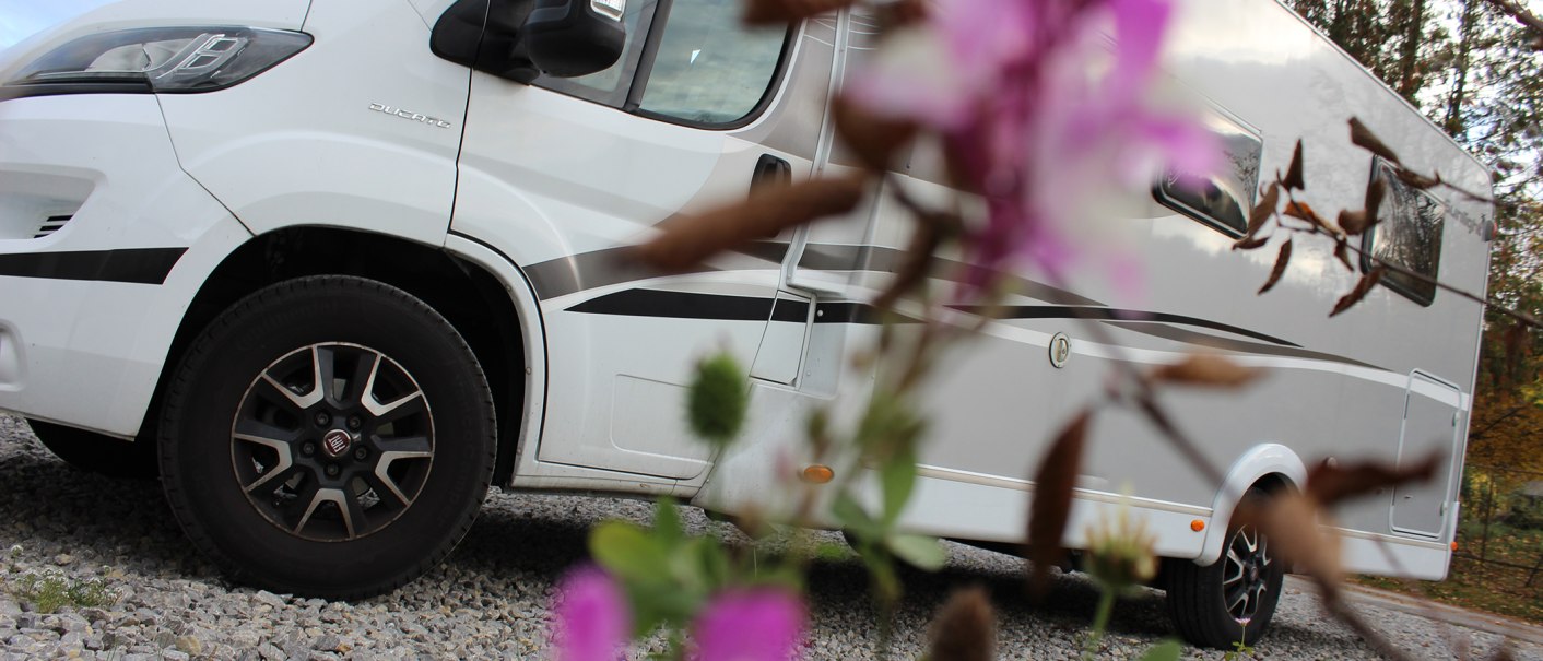 White motorhome on gravel parking lot, blurred flowers in the foreground. Side view with focus on the wheels., © Erlebnisregion Schwäbischer Albtrauf e. V.