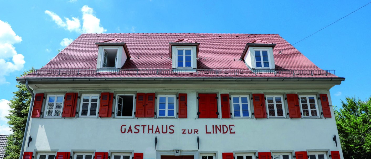 Das Gasthaus zur Linde hat rote Fensterläden und ein rotes Ziegeldach. Der Himmel ist blau mit wenigen Wolken., © Fei Shiyu