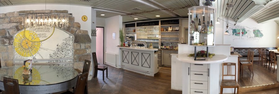 Rustic restaurant with wooden furniture, bar and decorative wall with "sun broom" motif. Cozy atmosphere with chandelier and wine rack., © Weingut Zaiß